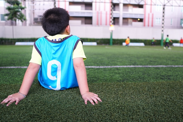 Asian young boy waiting on the junior football training.