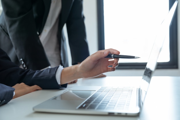 Asian young businesswoman using a pen point to marketing business plan on the laptop to show her manager in the work office