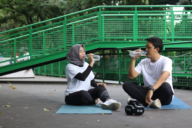 아시아 젊은 부부는 공원에서 요가 매트에서 운동한 후 물을 마신다