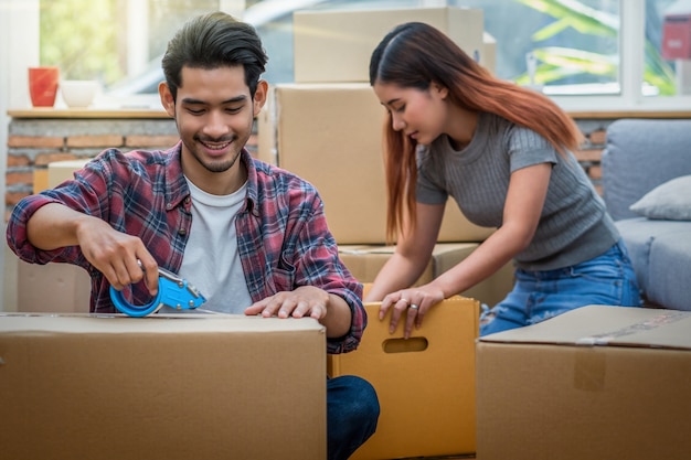 Asian young couple packing the big cardboard box for moving in new house