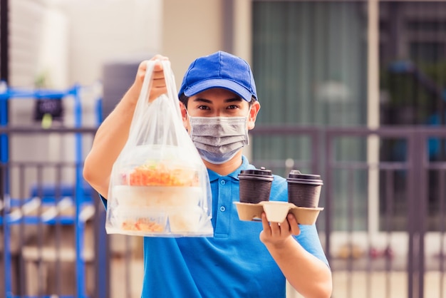 파란색 제복을 입은 아시아 젊은 배달원은 얼굴 마스크를 쓰고 대유행 코로나바이러스 아래 앞집에서 쌀 음식 상자 비닐봉지와 커피를 제공하는 식료품 서비스를 만들고 새로운 정상 개념으로 돌아갑니다.