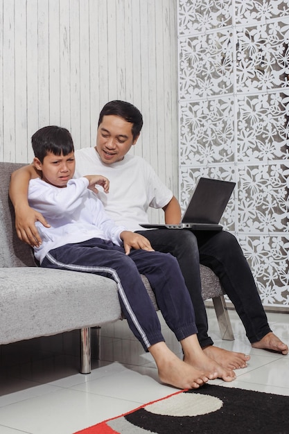 白いTシャツを着たアジアの若い父親は、ルの間に泣いているときに白いセーターを着た息子に元気を与えています