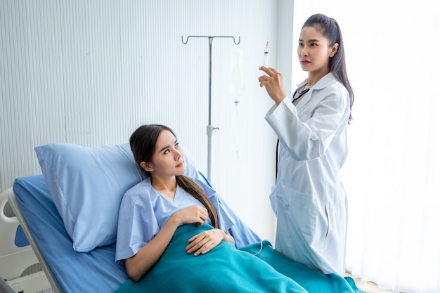 Asian young female doctor with syringe to Asian young female patient on Bed for better healing In the room hospital background.