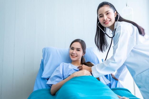 Giovane paziente asiatica sul letto mentre il medico controlla le mani esaminando il suo polso per registrare i risultati del trattamento con una faccina sorridente sintomo molto buono sullo sfondo dell'ospedale