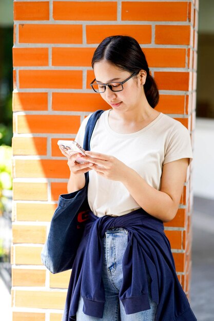 Asian young female student in casual cloth holding and play smart mobile at her school building