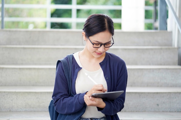 Asian young female student in casual cloth reading and make a short note on tablet for the exam