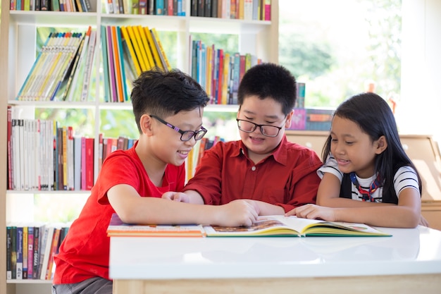 La ragazza asiatica & i libri di lettura dei ragazzi sullo scrittorio e sulla felicità ritengono alla biblioteca in loro scuola