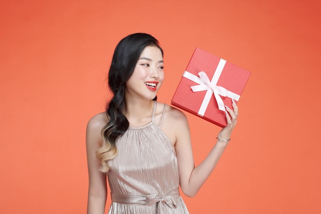 Asian young girl in dress holding red gift box with cheerful expression on background