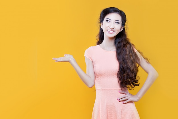 Asian young  girl  holding something in hand, place for your text. Portrait on yellow. 