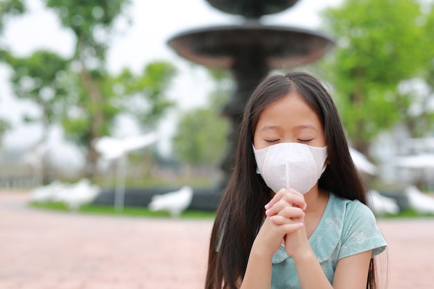 Asian young girl kid closed eyes with wearing face mask and pray gesture for stop covid19 during coronavirus outbreak