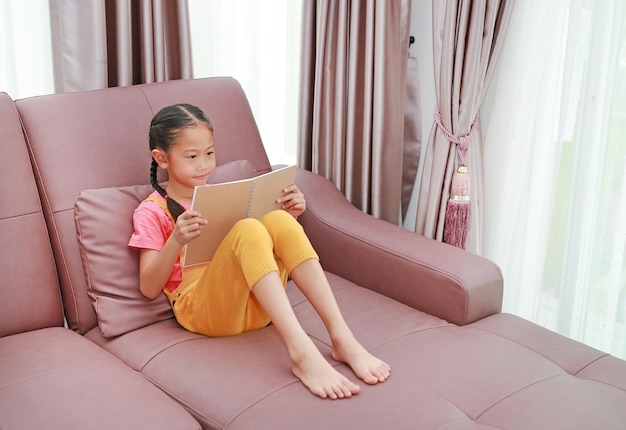 집에서 소파에 누워 책을 읽고 아시아 어린 소녀