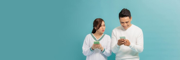 Молодая азиатская девушка шпионит за мобильным телефоном своего партнера на синем фоне