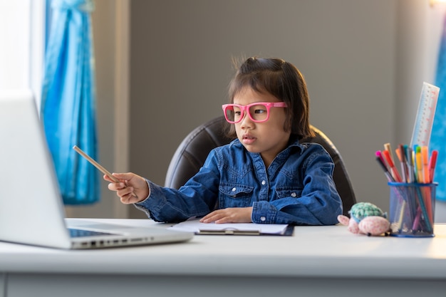 アジアの若い女の子はオンラインで勉強して家にいます病気の状況で