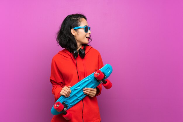 Asian young girl with skate over purple wall