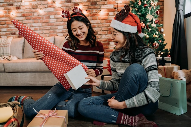 家で贈り物を包むのを楽しんでいるアジアの若い女の子。クリスマスのプレゼントを詰める友人の素晴らしいチームワーク。来る新年とクリスマスの準備。