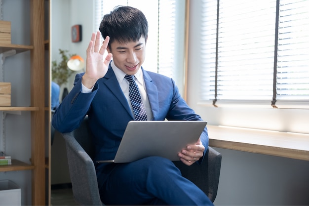 Giovane uomo bello asiatico che per mezzo del computer portatile