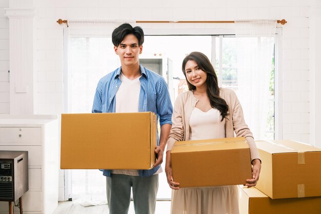 Asian young happy new married couple moving boxes parcel to their new house or real estate