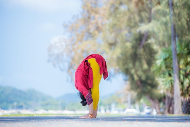 Photo asian young healthy woman posing practice bird of paradise yoga on stone beach with blue cloud sky