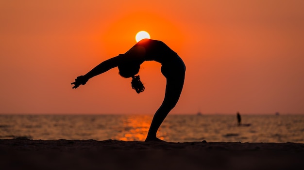 Asian young healthy woman posing practice bird of paradise yoga on stone beach with blue cloud sky