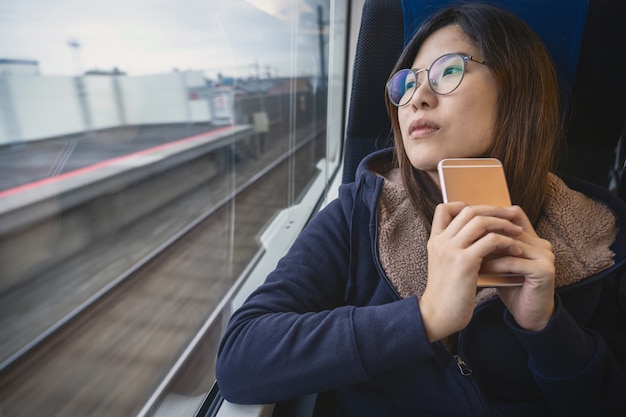 アジアの若い女性の乗客旅行中の電車の中の窓の横に落ち込んでいる気分に座っています。