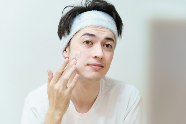 Asian young man applying cream to his face