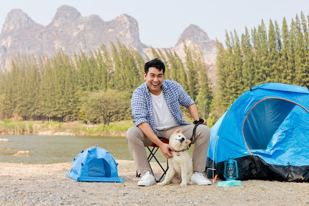 湖の丘でキャンプかわいい子犬犬と青いシャツを着てアジアの若い男山の景色の幸せと人生を楽しむ