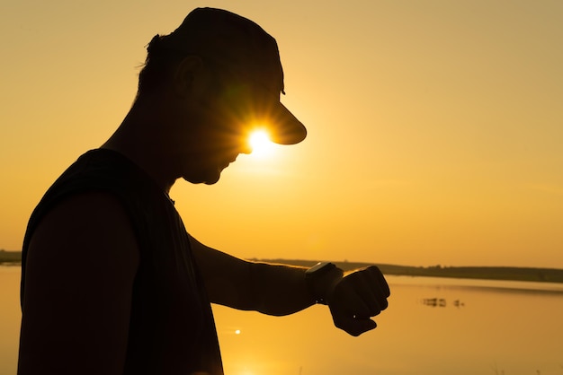 Giovane asiatico che controlla il tempo sull'orologio fitness dopo l'esercizio vicino al tramonto