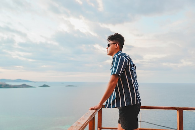 Asian young man enjoying the sea view from the balcony