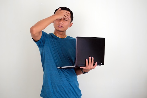 Asian young man holding his head while seeing on the laptop isolated on white background