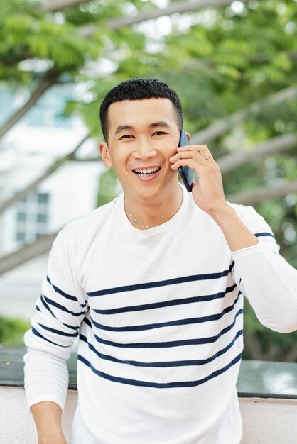 Asian young man looking at camera while talking on mobile phone in the city outdoors