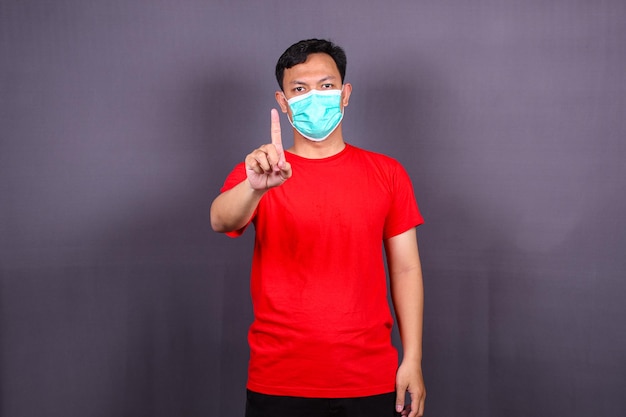 코비드-19에 대한 조치를 사용하도록 요청하는 얼굴 마스크를 가리키는 아시아 청년