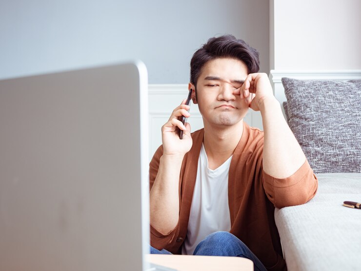 Photo asian young man rubbing his tired eyes his smartphone.