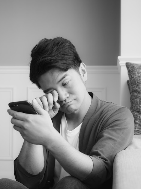 Asian young man rubbing his tired eyes his smartphone