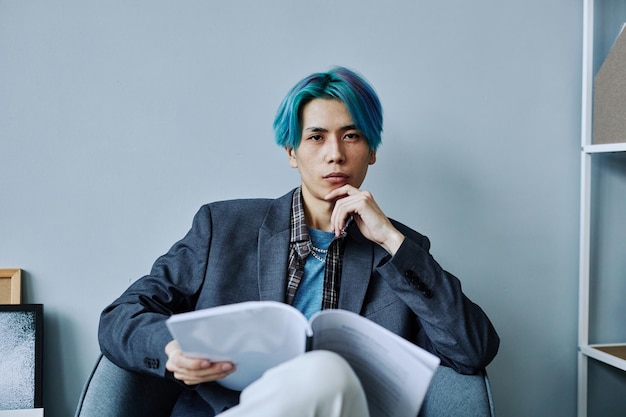 Asian young man sitting in chair in office and looking at camera with confidence