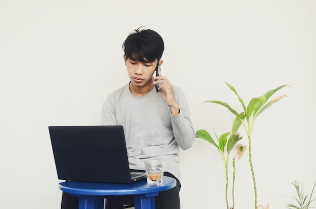 전화를 하는 동안 노트북 앞에 앉아 있는 아시아 청년