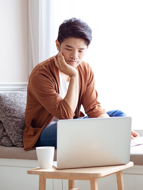 Asian young man sitting at the table in front of laptop computer