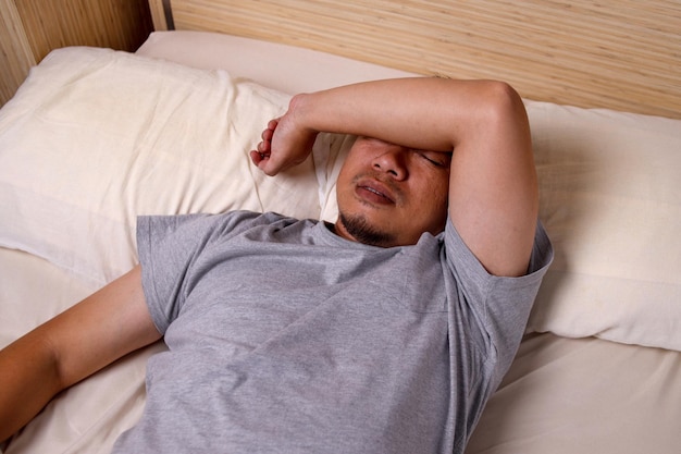 Азиатский молодой человек спит в белых постельных принадлежностях