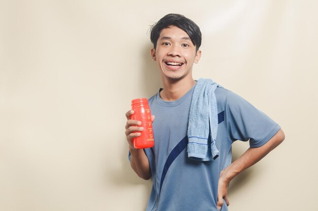 Asian young man in sports tshirt looking tired and drinking isolated on background