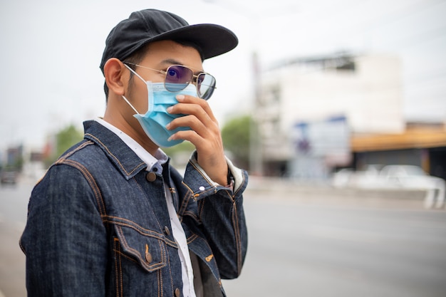Азиатский молодой человек стоял в городе и носить защитную маску на лице для защиты от загрязнения воздуха, твердых частиц и для защиты от вируса гриппа, гриппа, коронавируса в городе
