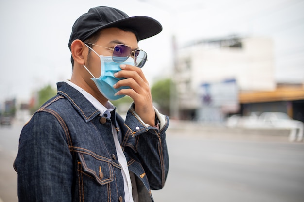 Asian Young man standing in the city and wearing protection mask on face for protection air pollution, particulates and for protection flu virus, influenza, coronavirus at city