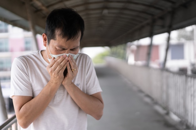 Il giovane asiatico indossa una maschera e tossisce dall'inquinamento atmosferico del pomeriggio 2.5