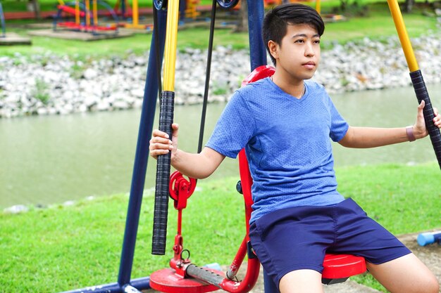 Asian young man wear the smart watch is exercising in park with outdoor exercise equipment