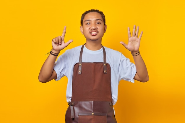 Asian young man wearing apron pointing with finger number seven with angry expression