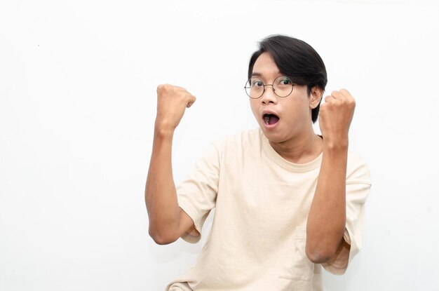 Азиатский молодой человек в повседневной бежевой футболке удивлен, поражен, вау, потрясен, поднимая руки да жест