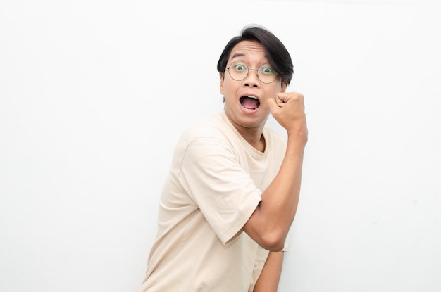 Asian young man wearing casual beige tshirt surprised, amazed, wow shocked raising arms yes gesture