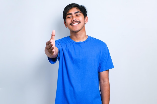 Asian young man wearing casual clothes smiling friendly offering handshake as greeting and welcoming over white background. successful business.
