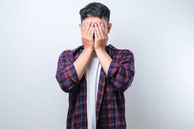 Asian young man wearing casual shirt with sad expression covering face with hands while crying depression concept