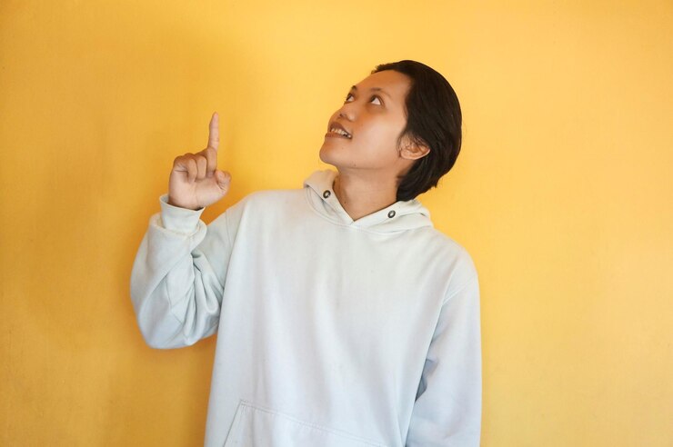 Photo ハウディを着たアジアの若い男が興奮して手の指を上に指さしている
