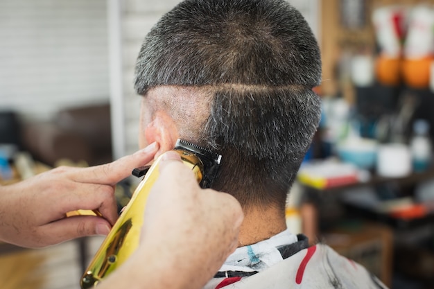 Asian young man who have gray hair being haircut with electric clipper machine by professional barber in barbershop.