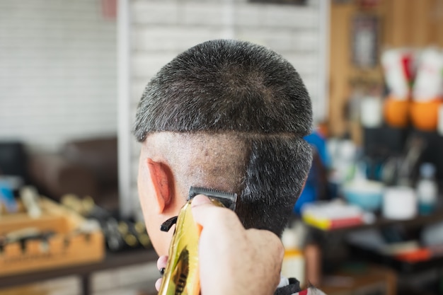 Giovane asiatico che ha i capelli grigi essendo taglio di capelli con tagliatore elettrico dal barbiere professionista nel negozio di barbiere.